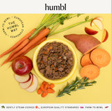 Bowl of humbl Country Chicken gently cooked dog food surrounded by fresh carrots, sweet potato, apple, and rosemary