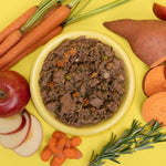 Bowl of humbl Country Chicken gently cooked dog food surrounded by fresh carrots, sweet potato, apple, and rosemary